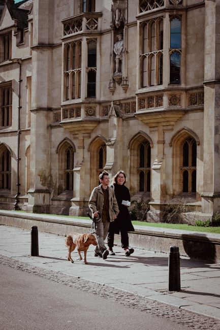 Couple strolling with dog near gothic building, showcasing urban life and historic architecture.