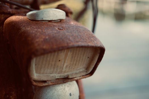 Detailed close-up of an old, rusty bicycle headlight with blurred background.