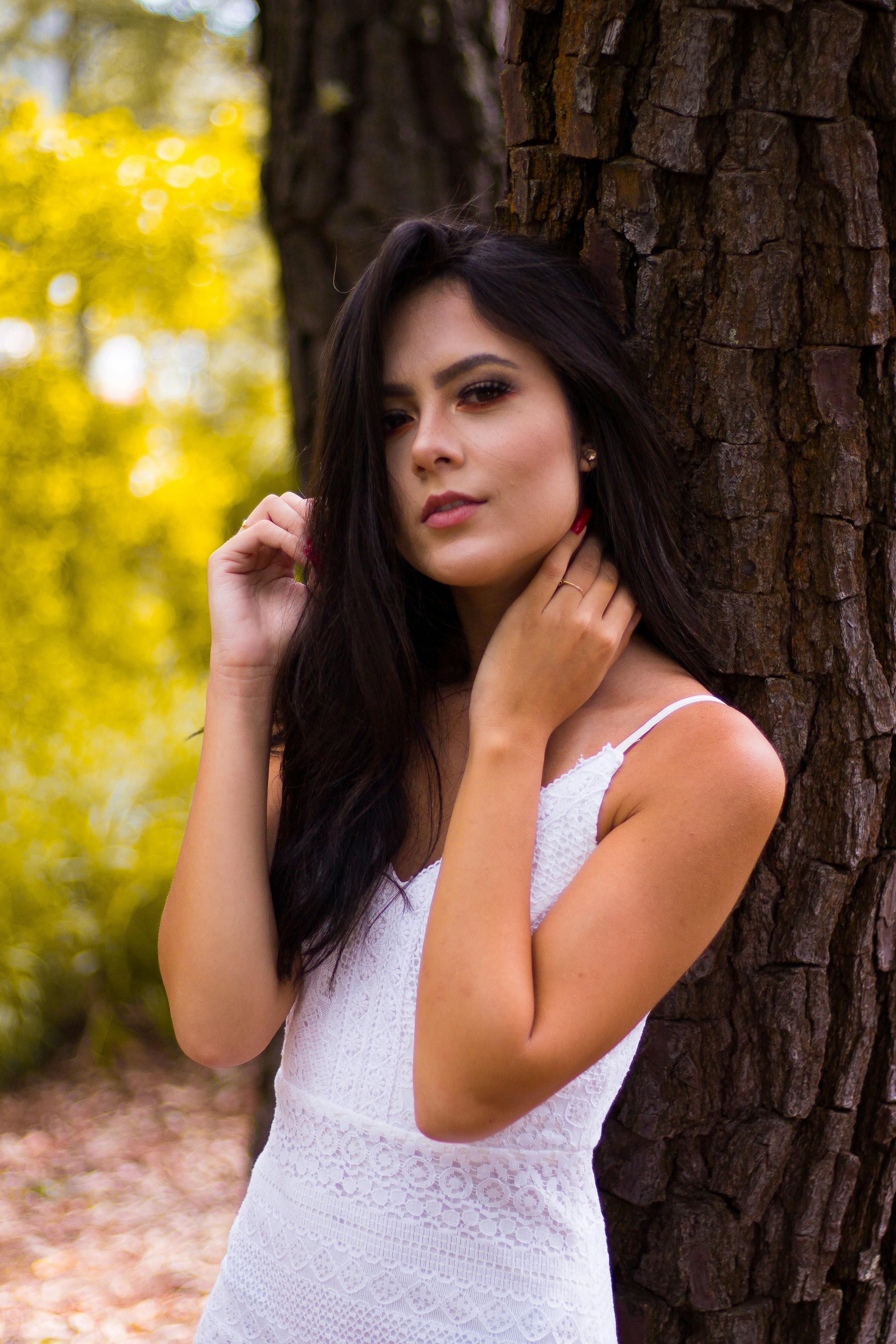 一位时尚的女士在阳光明媚的森林里，倚着树干摆姿势，展现自然之美