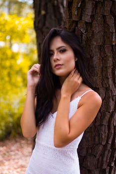 一位时尚的女士在阳光明媚的森林里，倚着树干摆姿势，展现自然之美