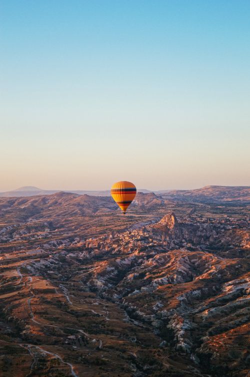 Free Stunning aerial view of a hot air balloon floating over Cappadocia's unique landscape at sunrise. Stock Photo