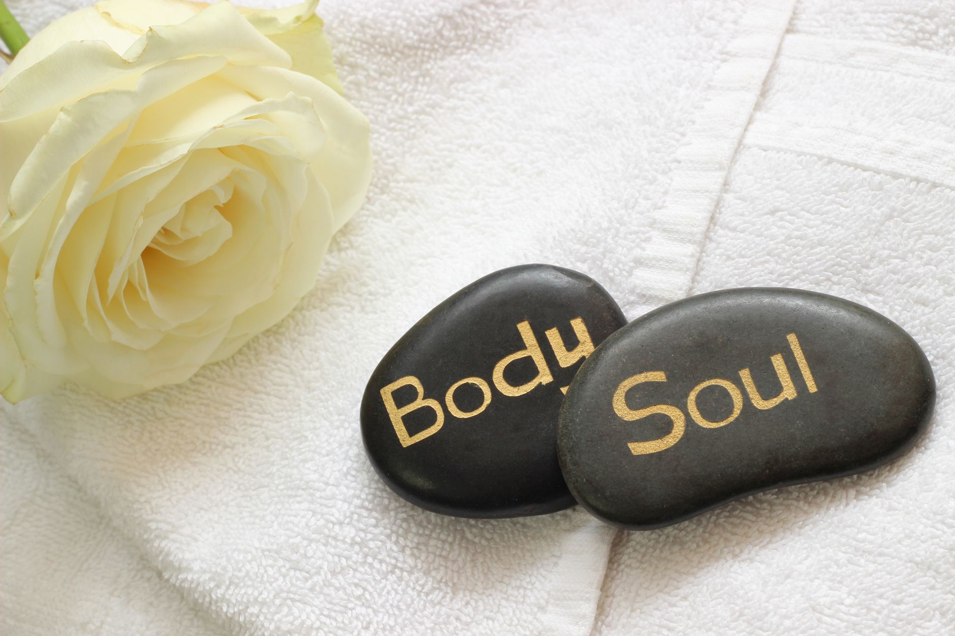 Master Gua Sha Face Techniques For A Glowing Skin 1 Tranquil spa arrangement featuring a white rose and engraved stones on a towel for relaxation.