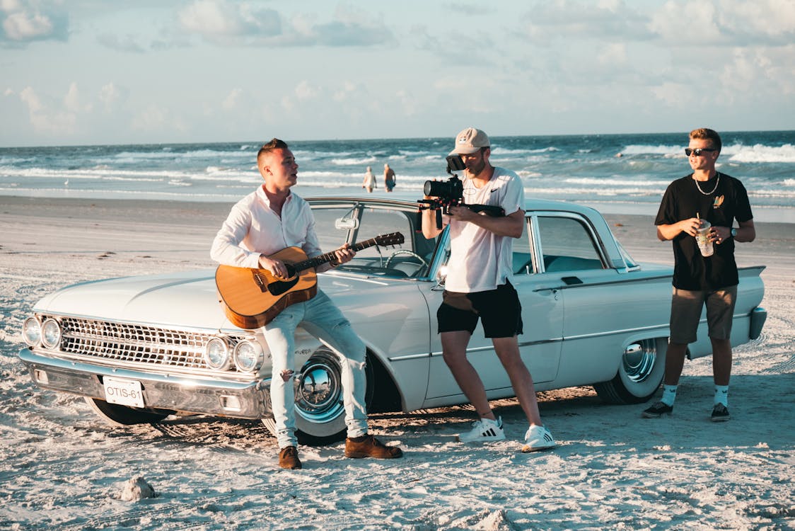 Three Men Near White Sedan on Shore