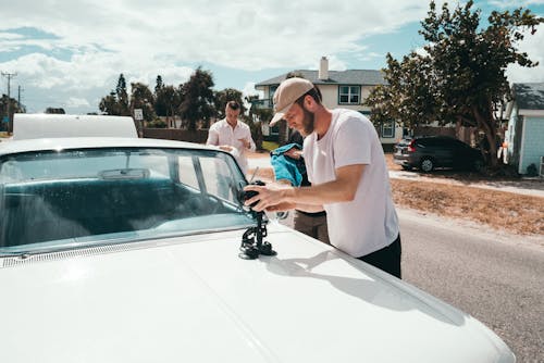 Man Wears White Crew-neck T-shirt Holding Camera on White Vehicle