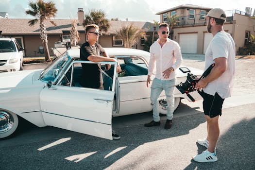 Three men with camera equipment near a classic car on a sunny day, showcasing filming outdoors.