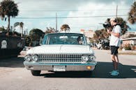 电影制片人在阳光明媚的城市街道上，手持相机拍摄了一辆老爷车