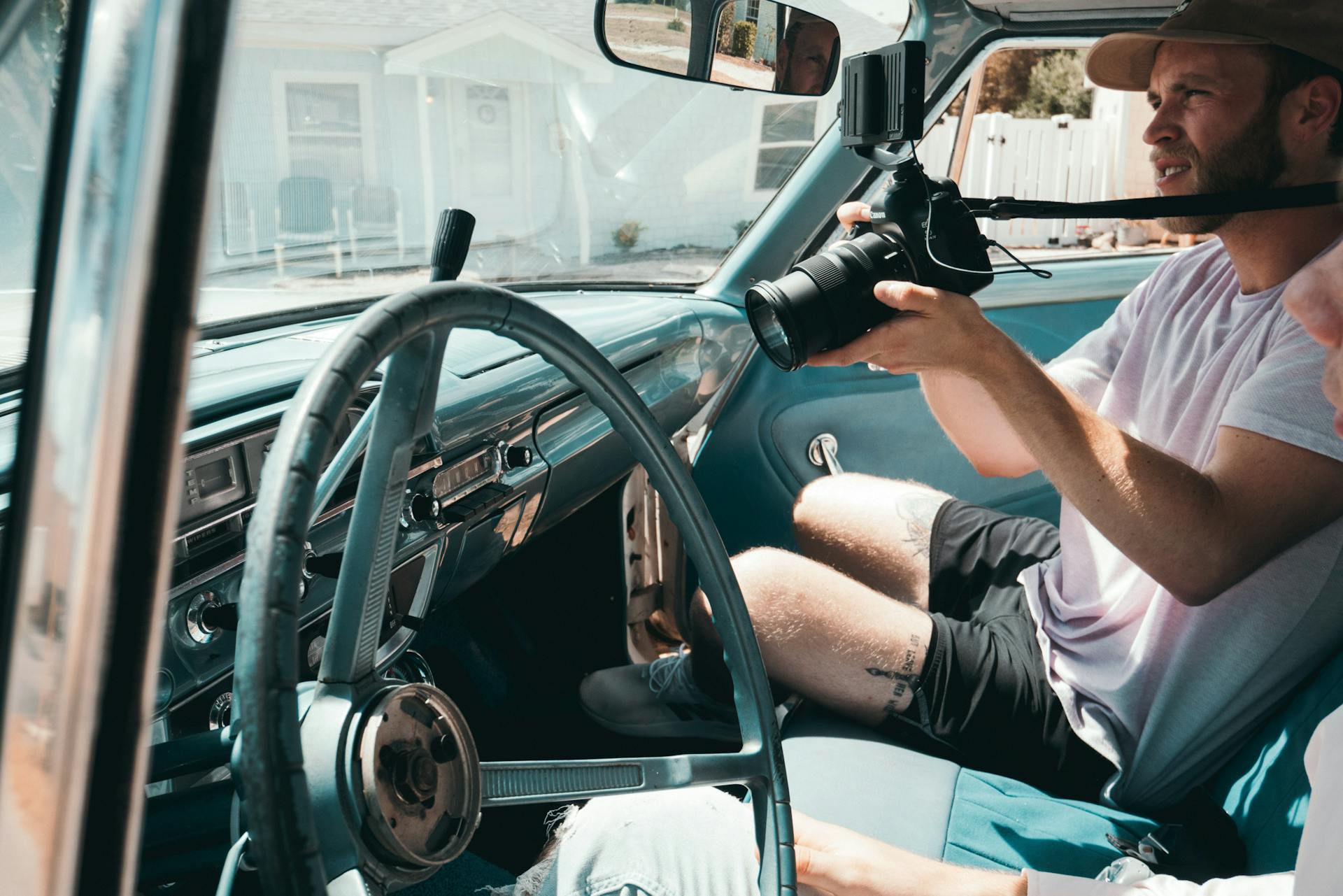 A man filming with a camera inside a vintage car during the day.