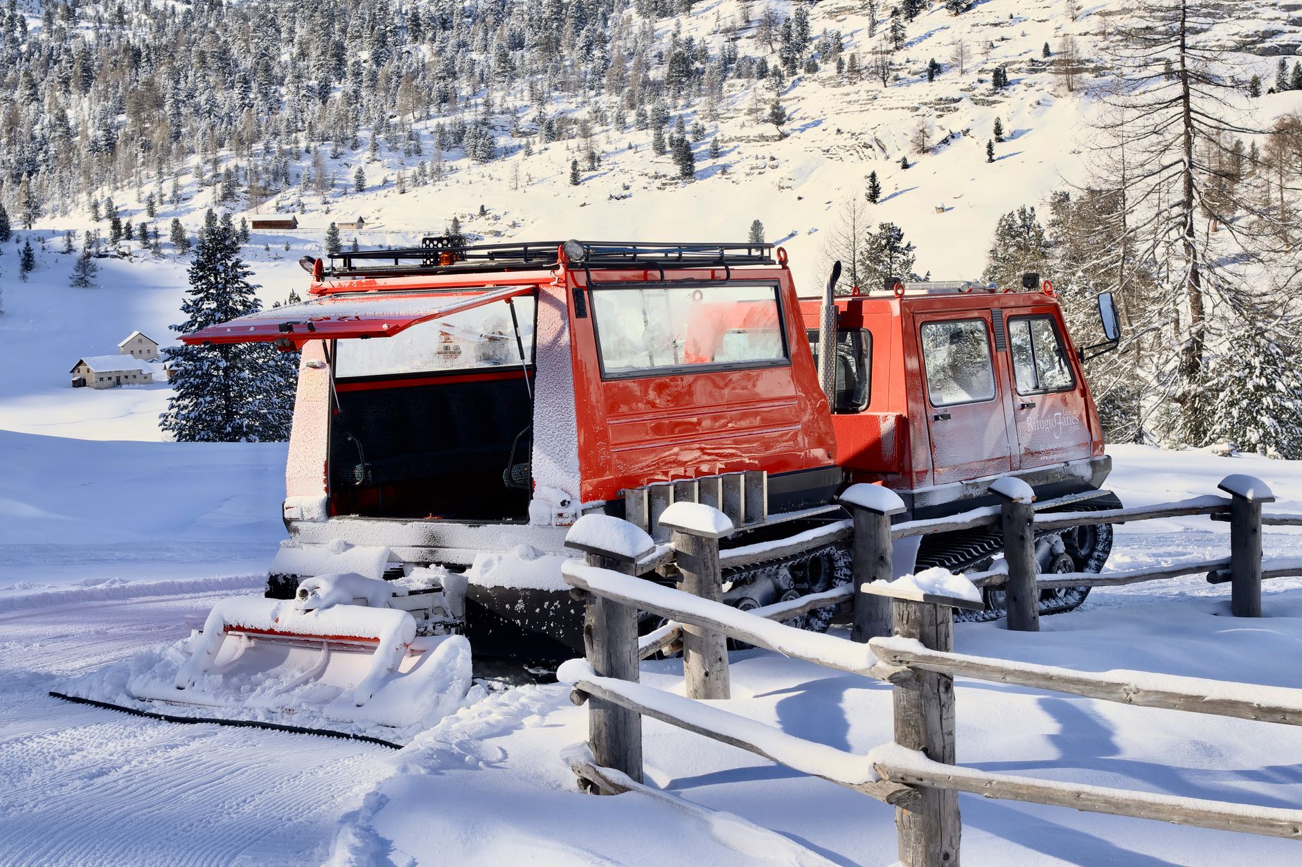 Red snowcat in a snowy San Vigilio landscape under bright daylight.