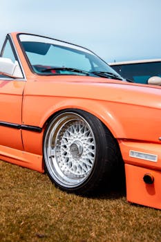 Vintage orange convertible car with custom wheels parked outdoors.