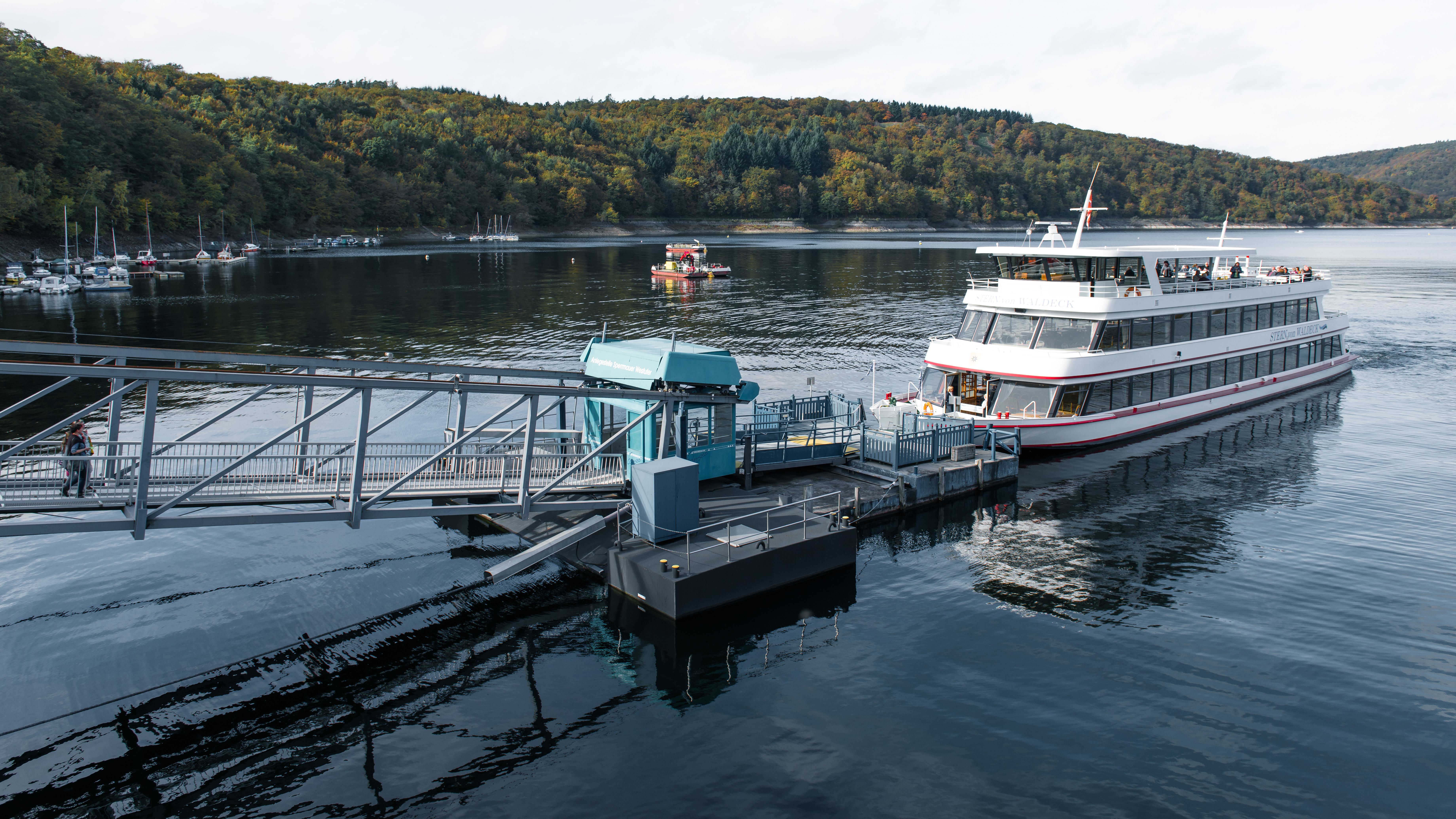 Ferry docked on a calm lake surrounded by dense green trees.