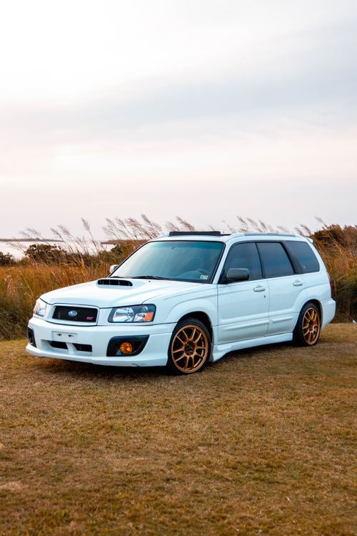 Free White car with gold wheels parked in an open field with a scenic background, captured during the day. Stock Photo