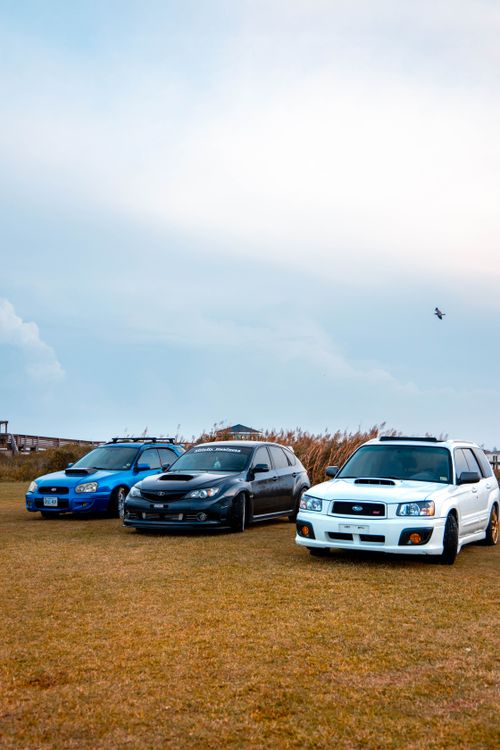 Free A stunning view of three cars parked on a grassy field under a cloudy sky, showcasing summer adventure. Stock Photo