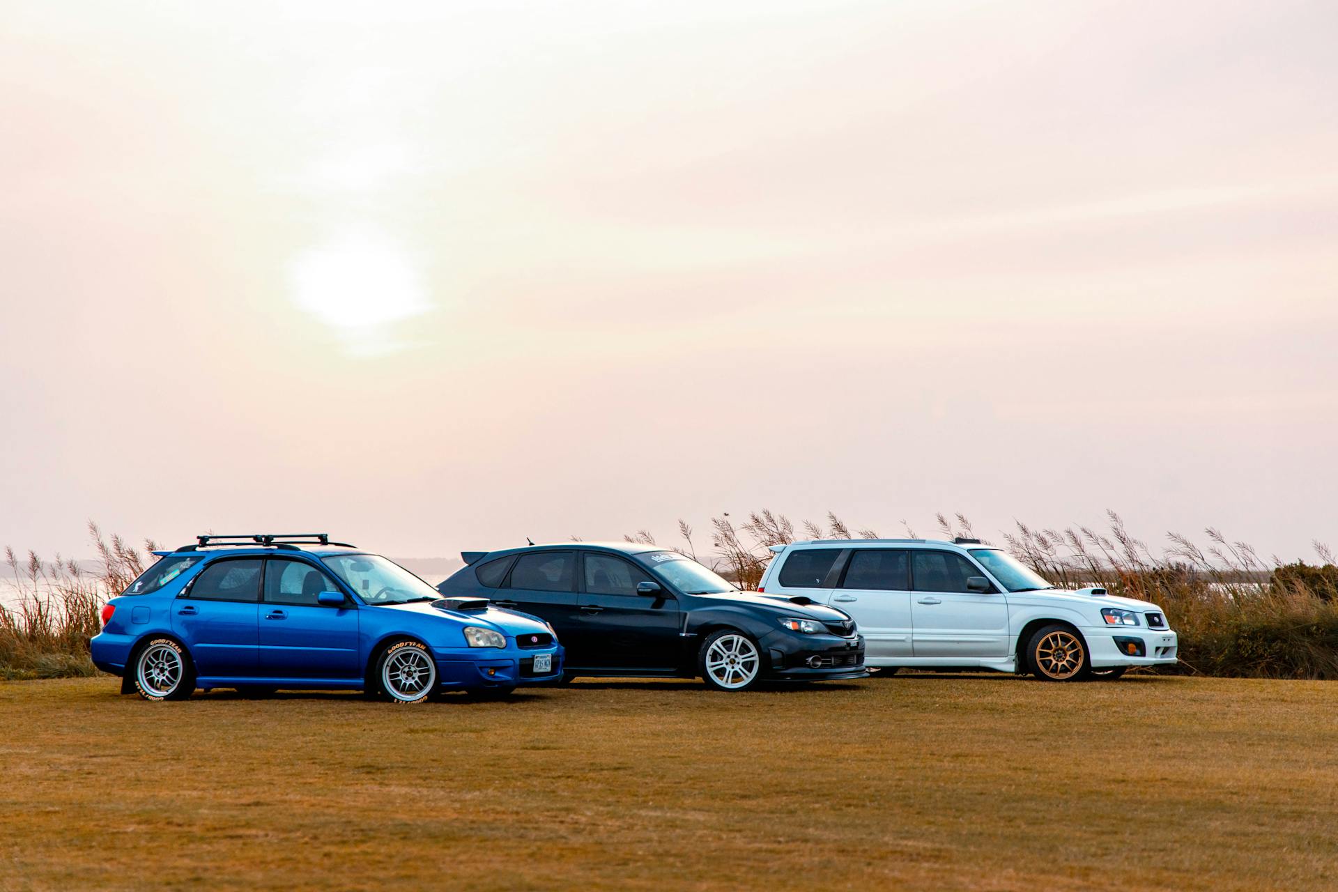 A trio of cars parked on grass with a scenic sunset background.