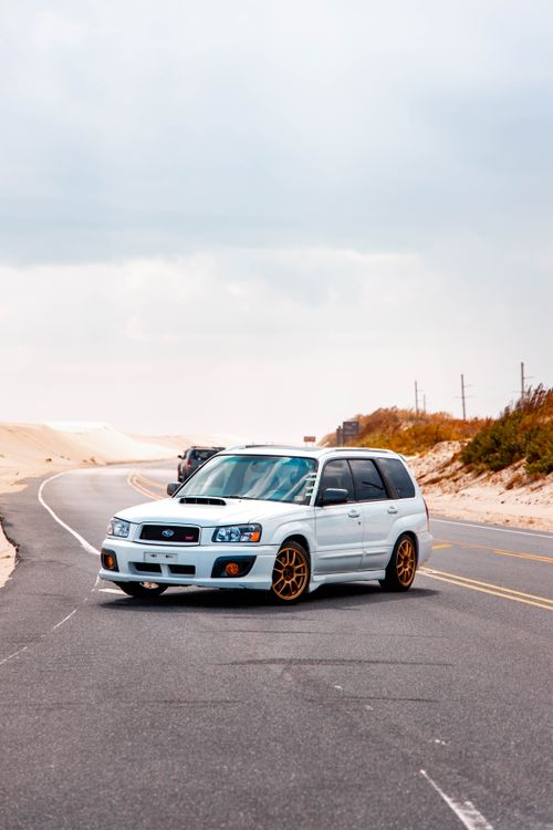 Free White SUV parked on a winding road near desert dunes under a cloudy sky. Stock Photo