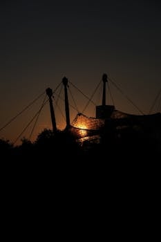 Silhouetted structures create a dramatic scene against the warm hues of a sunset sky.