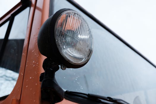 Detailed close-up of a vintage vehicle headlight with raindrops on orange exterior.