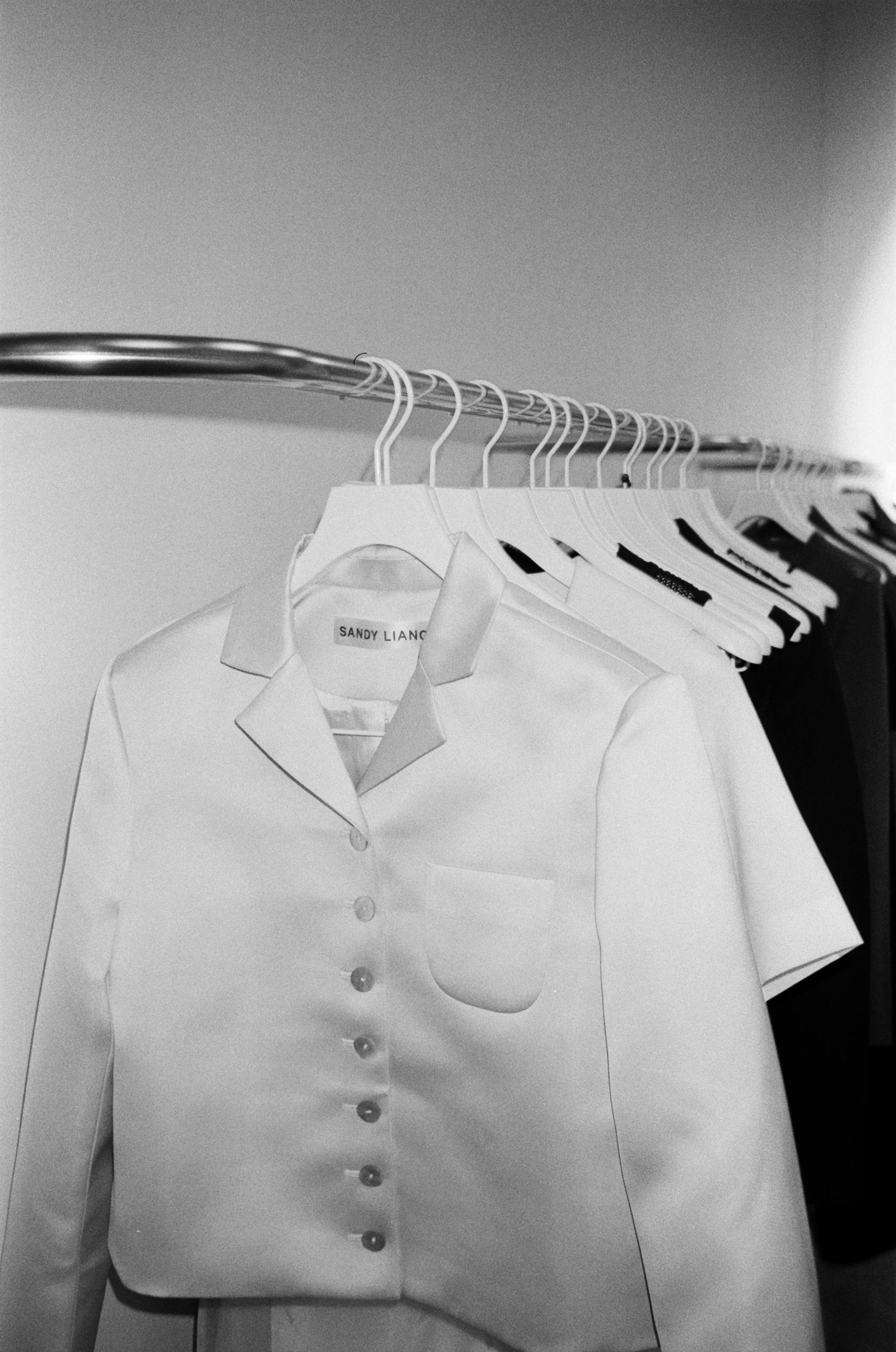 Black and white photo of elegant clothes on hangers in a store display.