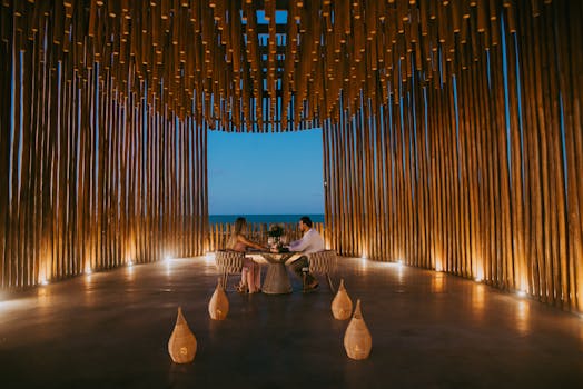 A couple enjoys a romantic dinner in a stylish oceanfront pavilion at twilight.