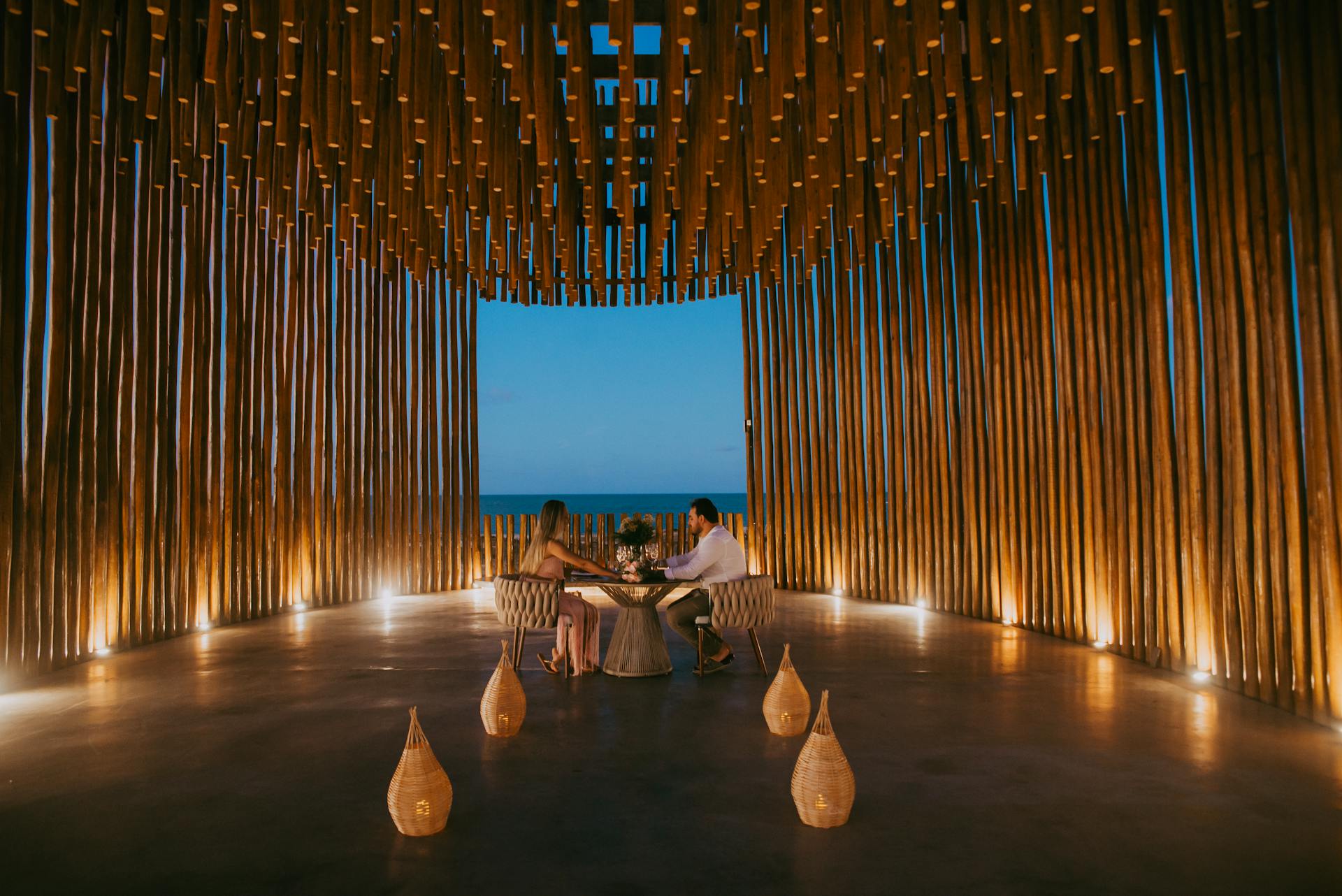 A couple enjoys a romantic dinner in a stylish oceanfront pavilion at twilight.