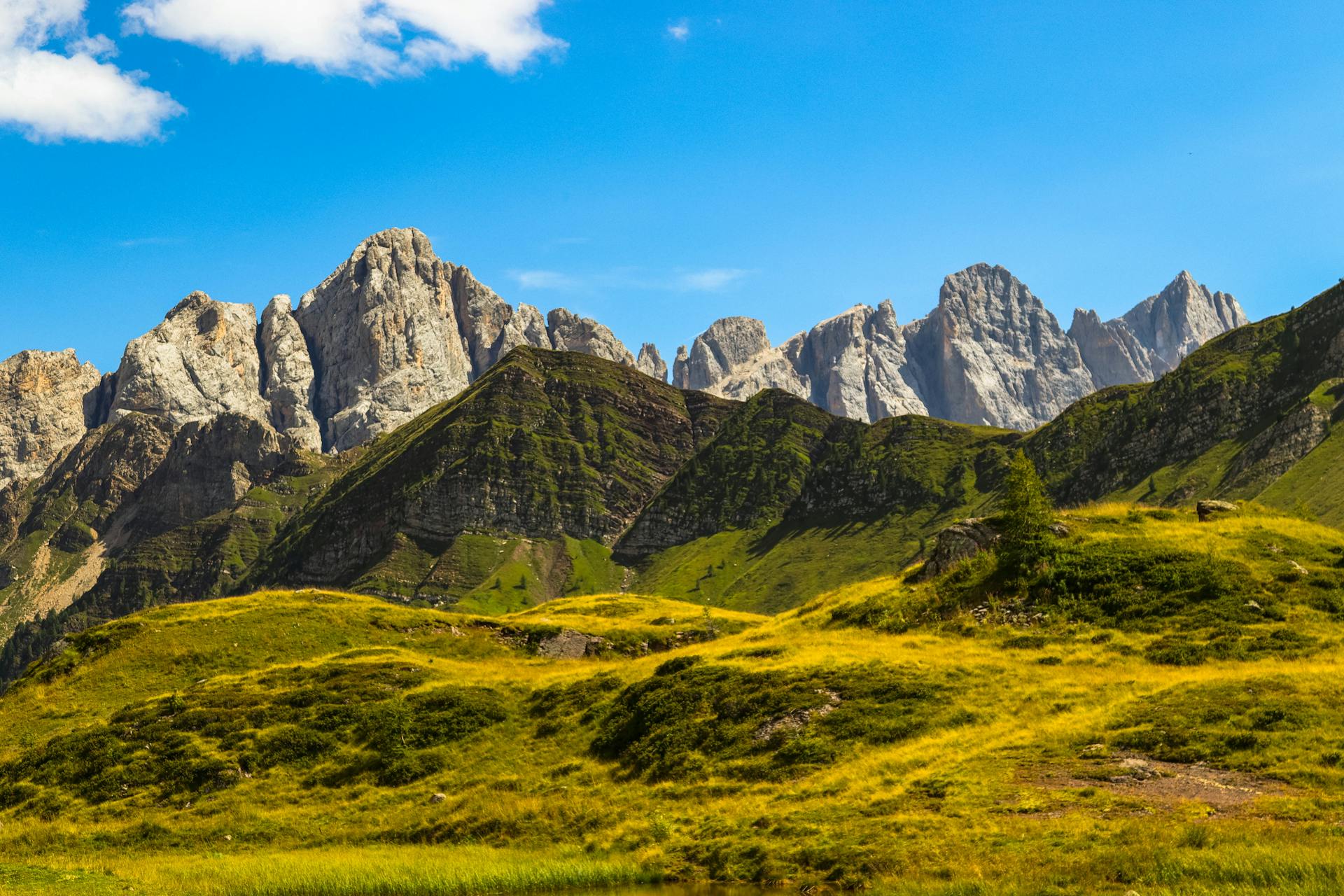 Scenic landscape of the Dolomites with vibrant green hills and clear blue sky, showcasing natural beauty.