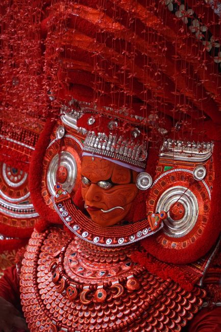 Close-up of a traditional Theyyam performer in intricate red costume in Kerala, India.