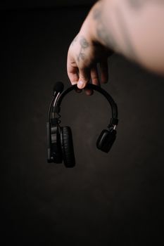 Artistic shot of black headphones suspended by a tattooed hand, creating a moody atmosphere.