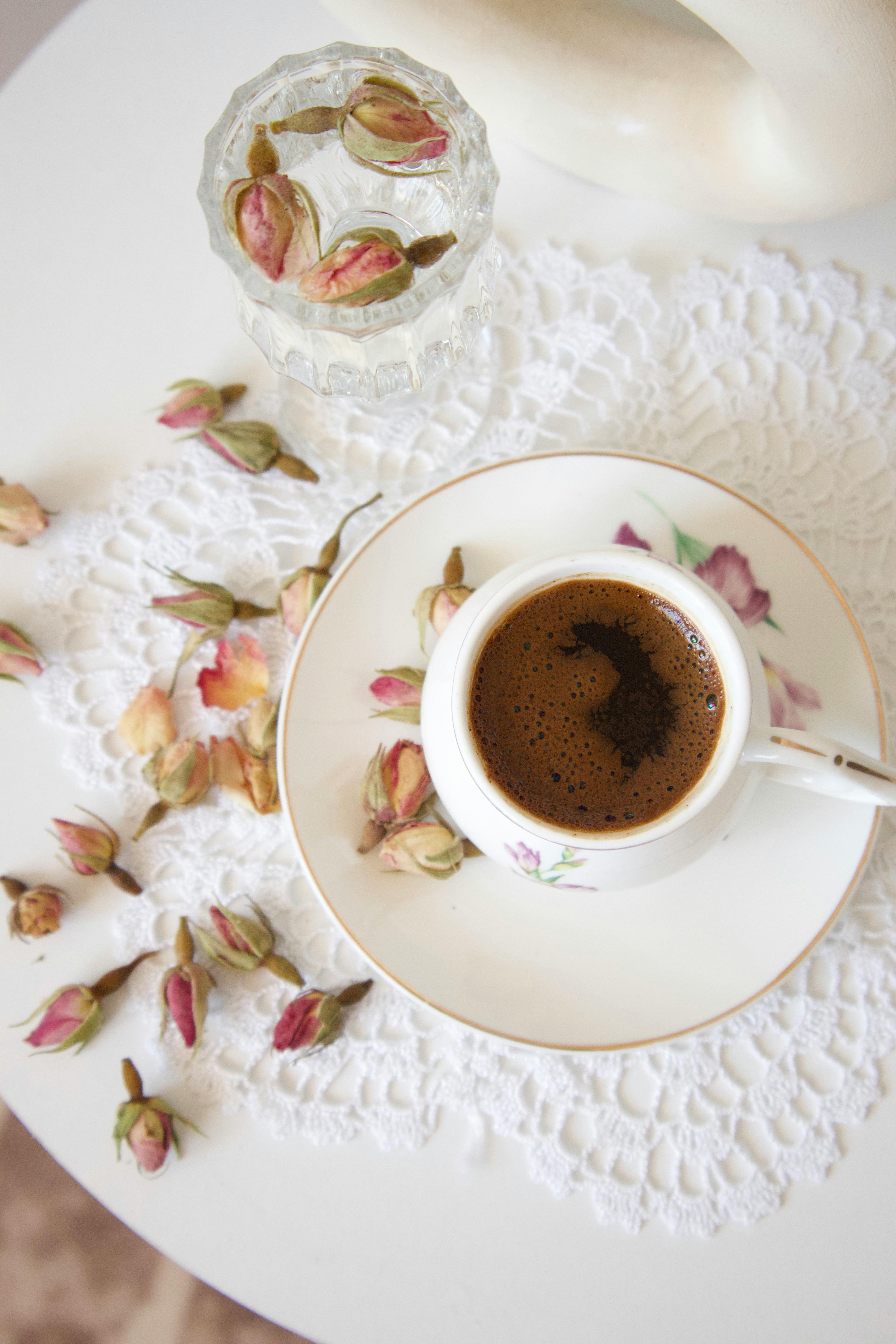 Delicate coffee cup on lace with rose petals for a cozy vibe.