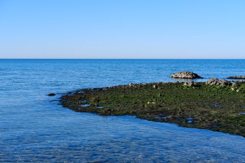 Free Peaceful ocean scene with rocky shore and vibrant blue sky, perfect for nature themes. Stock Photo