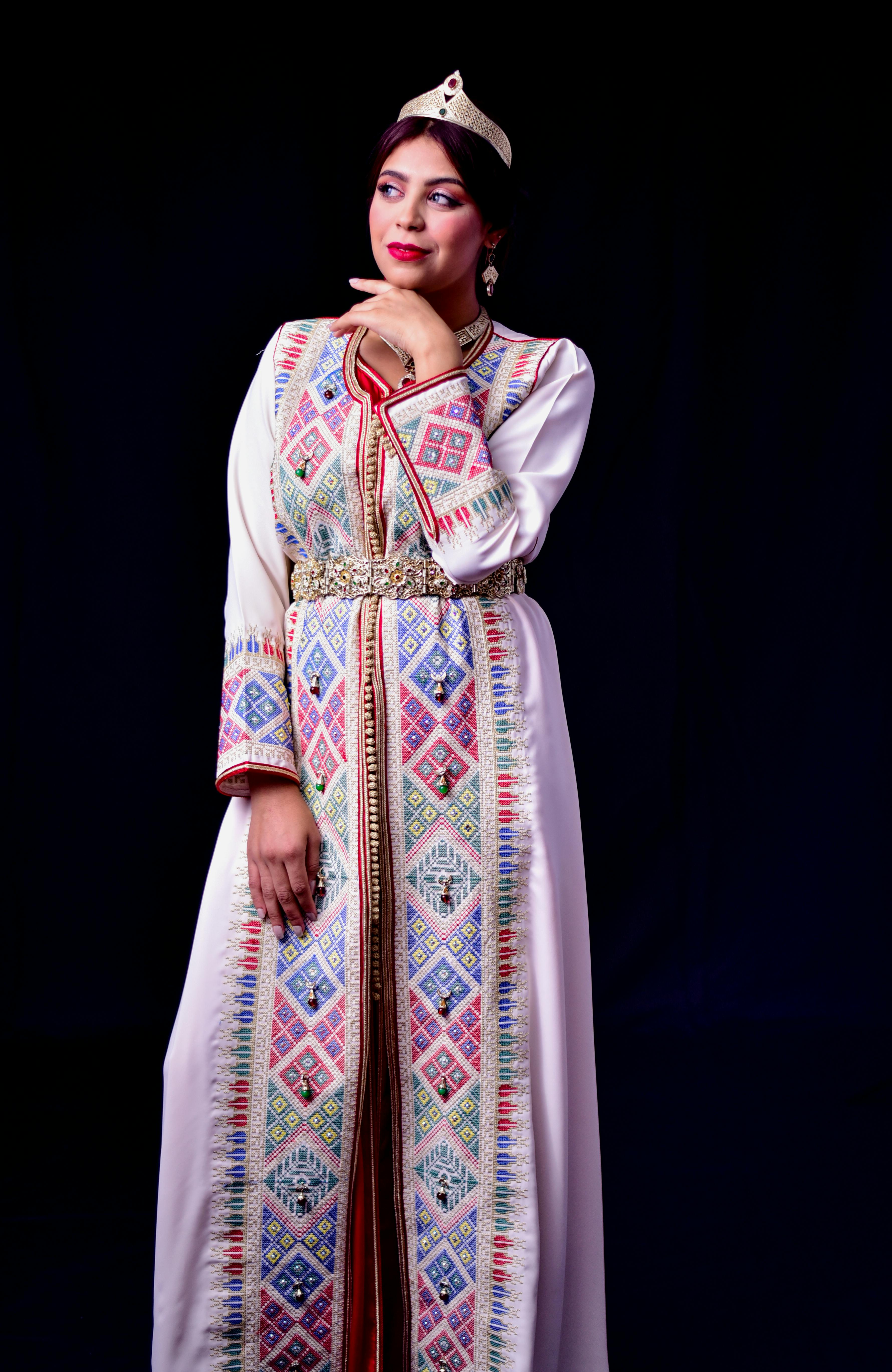 A woman poses elegantly in a colorful traditional Moroccan dress and crown.