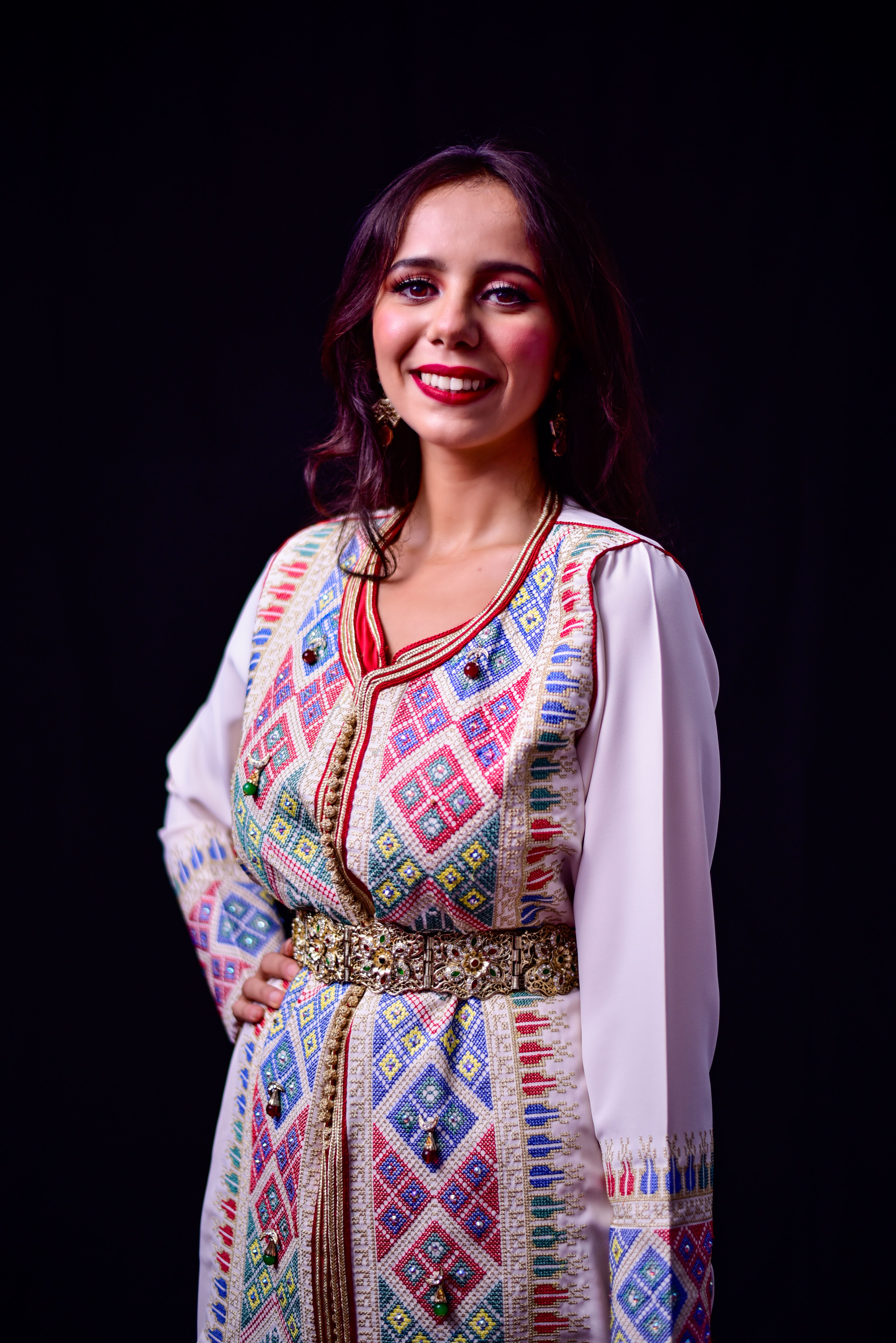 Portrait of a smiling woman in a colorful traditional Moroccan dress with intricate patterns.