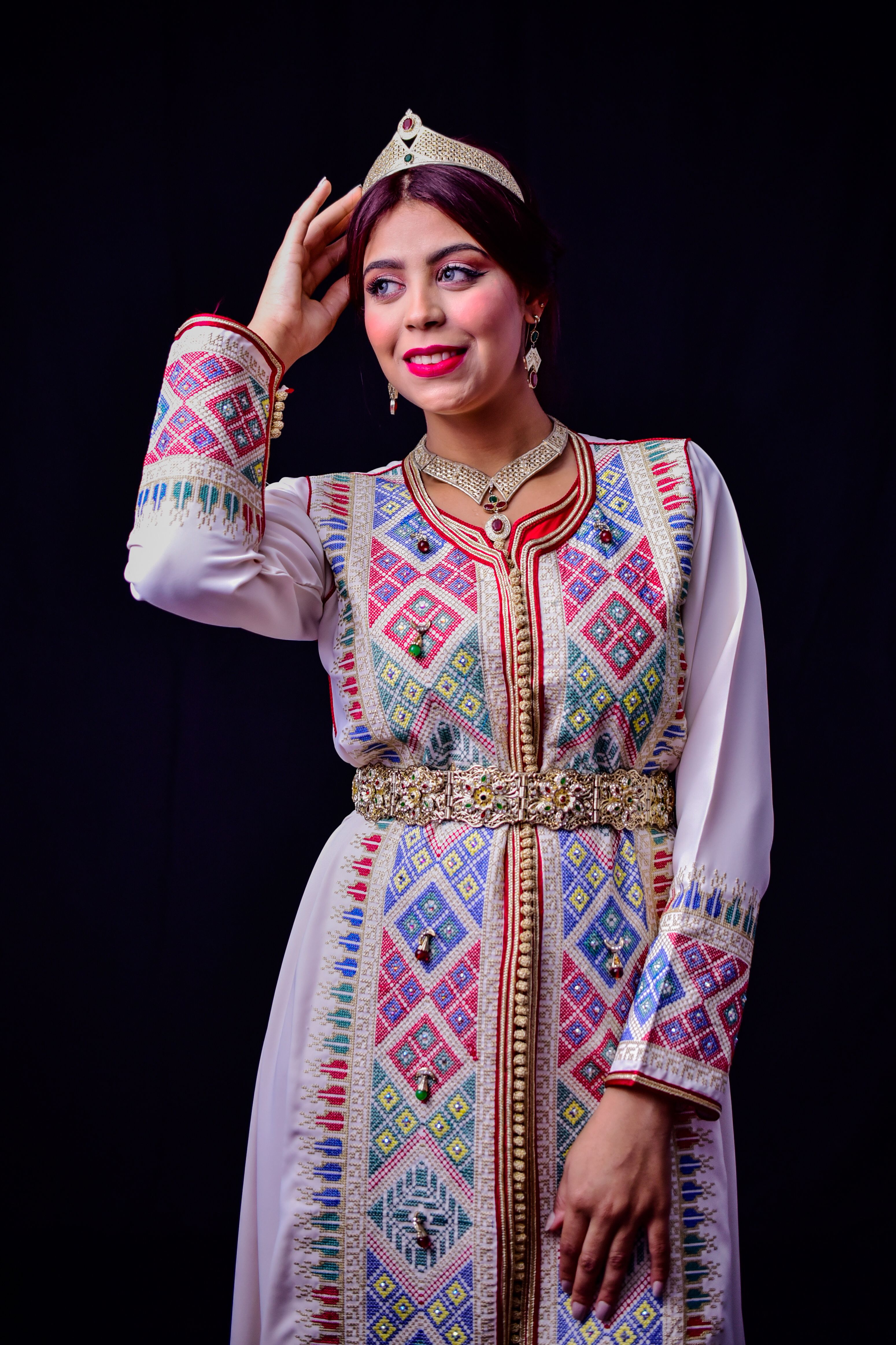 Elegant Moroccan woman in traditional kaftan and tiara on black background.
