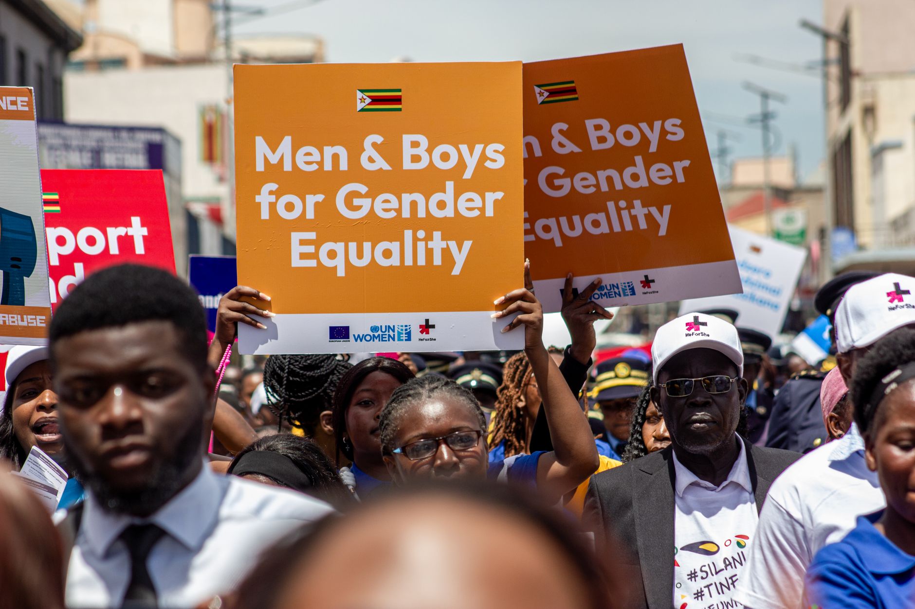 A vibrant crowd in Harare rallies for gender equality, holding signs promoting inclusion.