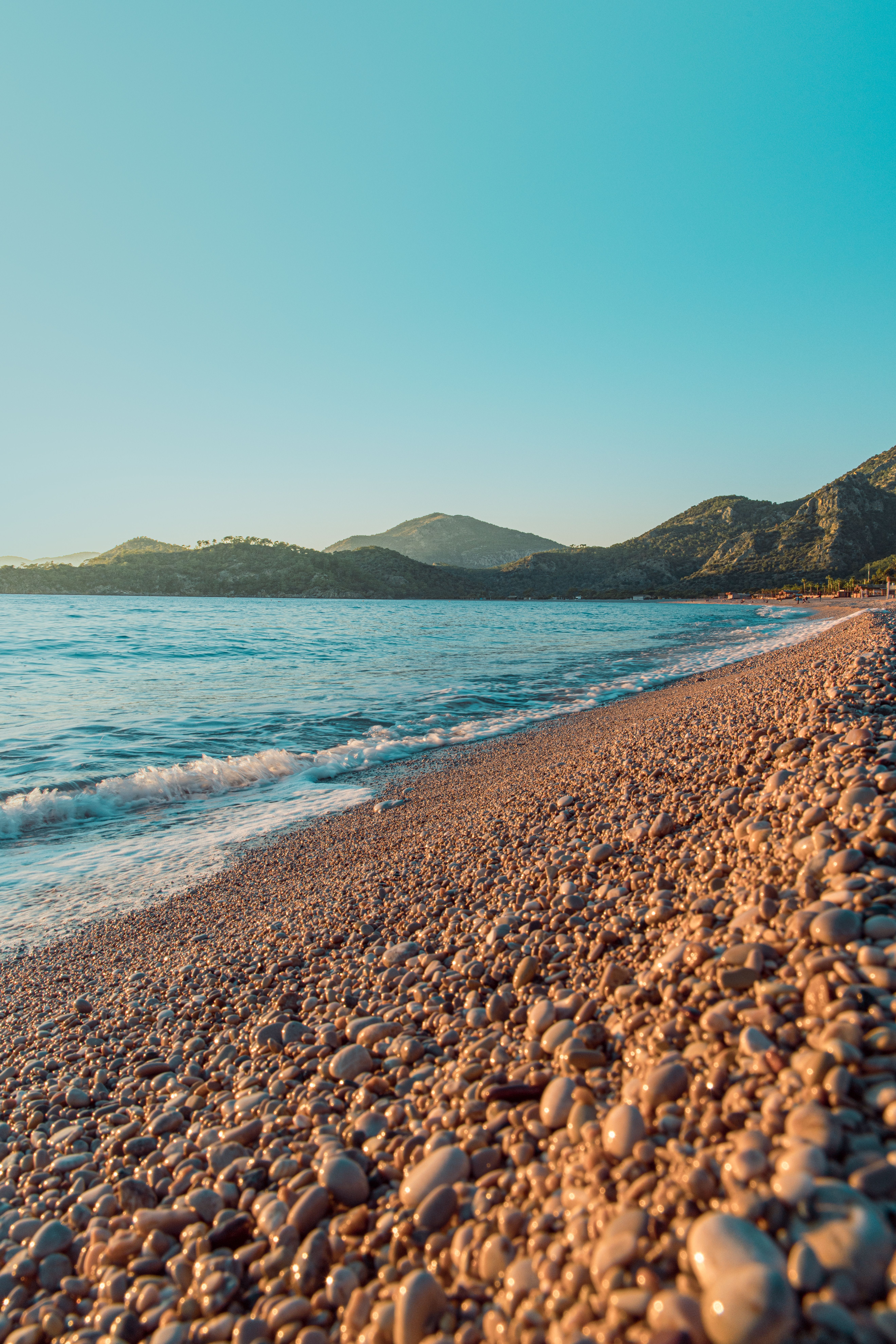 Serene Sunset Over Rocky Beach and Mountains · Free Stock Photo