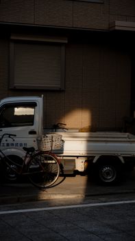 A shadowed street scene in Tokyo featuring a white truck and bicycle in warm evening light.