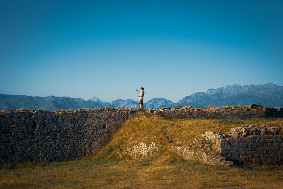 A solitary figure atop a historic castle wall in Albania during a vibrant sunset.