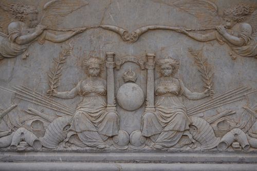Free Detailed stone carving depicting allegorical figures with laurel wreaths and ancient symbols. Stock Photo