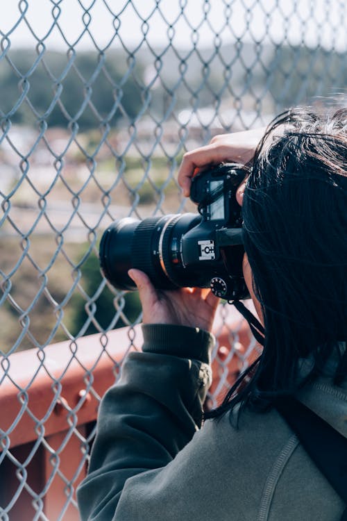 Woman Holding Dslr Camera Taking A Photo Behind A Wire Mesh Fence