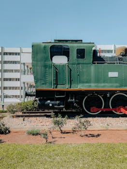 A vintage green locomotive displayed outdoors in urban Morocco, showcasing railway heritage amid modern architecture.