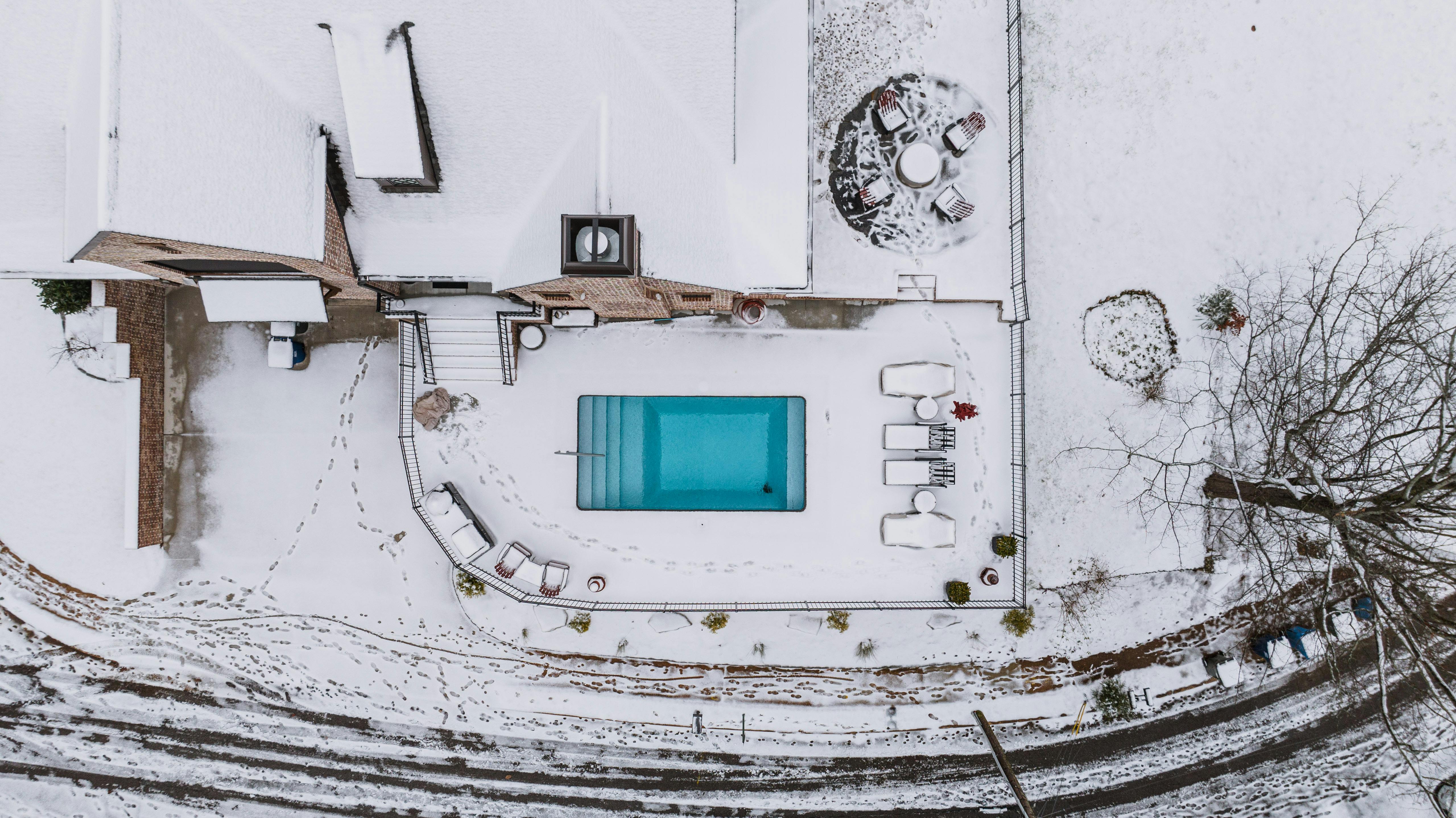 An aerial image capturing a house and pool covered in winter snow, creating a serene contrast.
