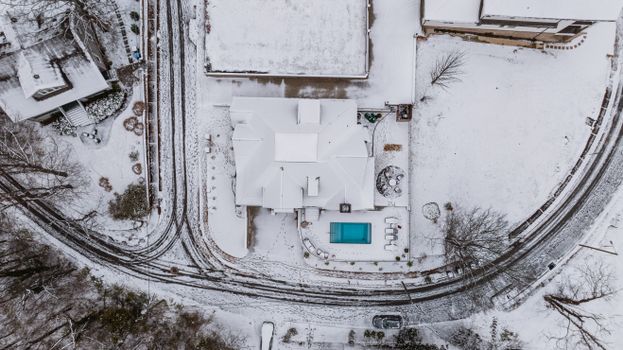 Aerial photograph capturing a snow-covered suburban neighborhood with visible houses and a pool.