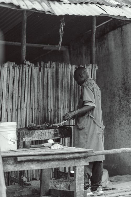 Free Black and white image of a chef grilling skewers at a street food stall in Bujumbura, Burundi. Stock Photo