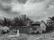 A rustic stone house surrounded by lush greenery in rural Bujumbura under an overcast sky.