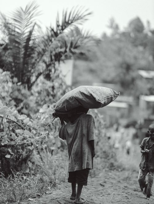 Free Black and white photo of a child carrying a large bag on their head in rural Burundi. Stock Photo