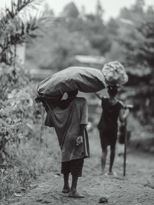 Free Black and white image capturing daily life in rural Burundi with people carrying goods along a dirt path. Stock Photo