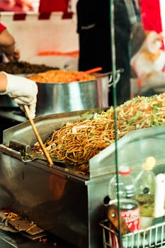 Street food stall in São Paulo with vendor cooking noodles in vibrant outdoor setting.