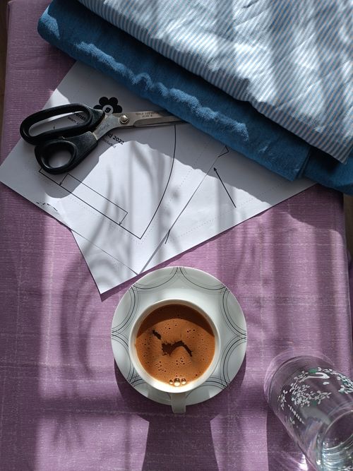 Free A creative workspace with sewing patterns, fabric, and coffee on a sunny day. Stock Photo