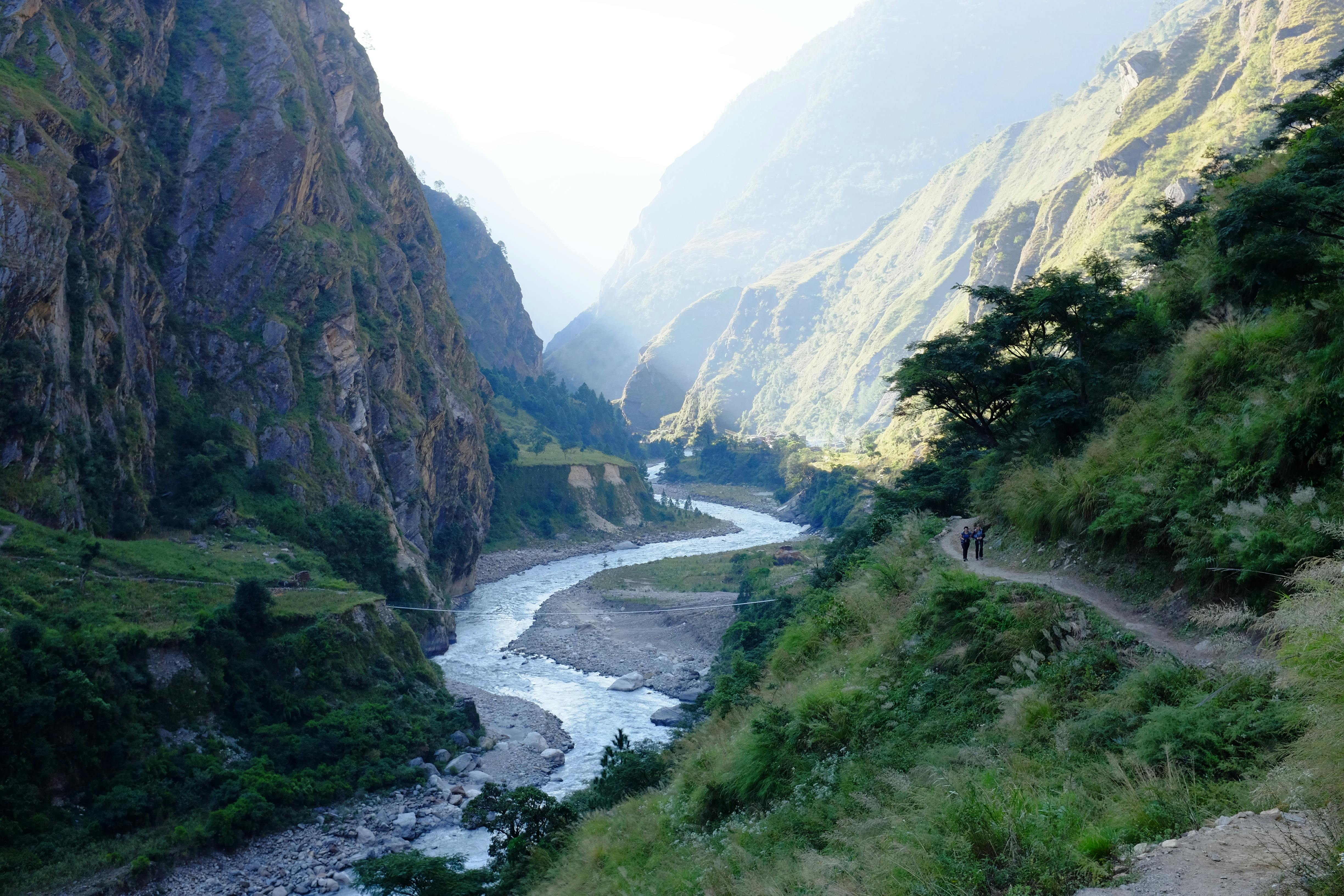 Breathtaking view of a river cutting through a lush valley in the Himalayas, ideal for trekking.