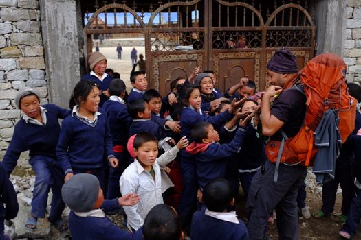 A group of schoolchildren enthusiastically gather around a trekker in rural Nepal.