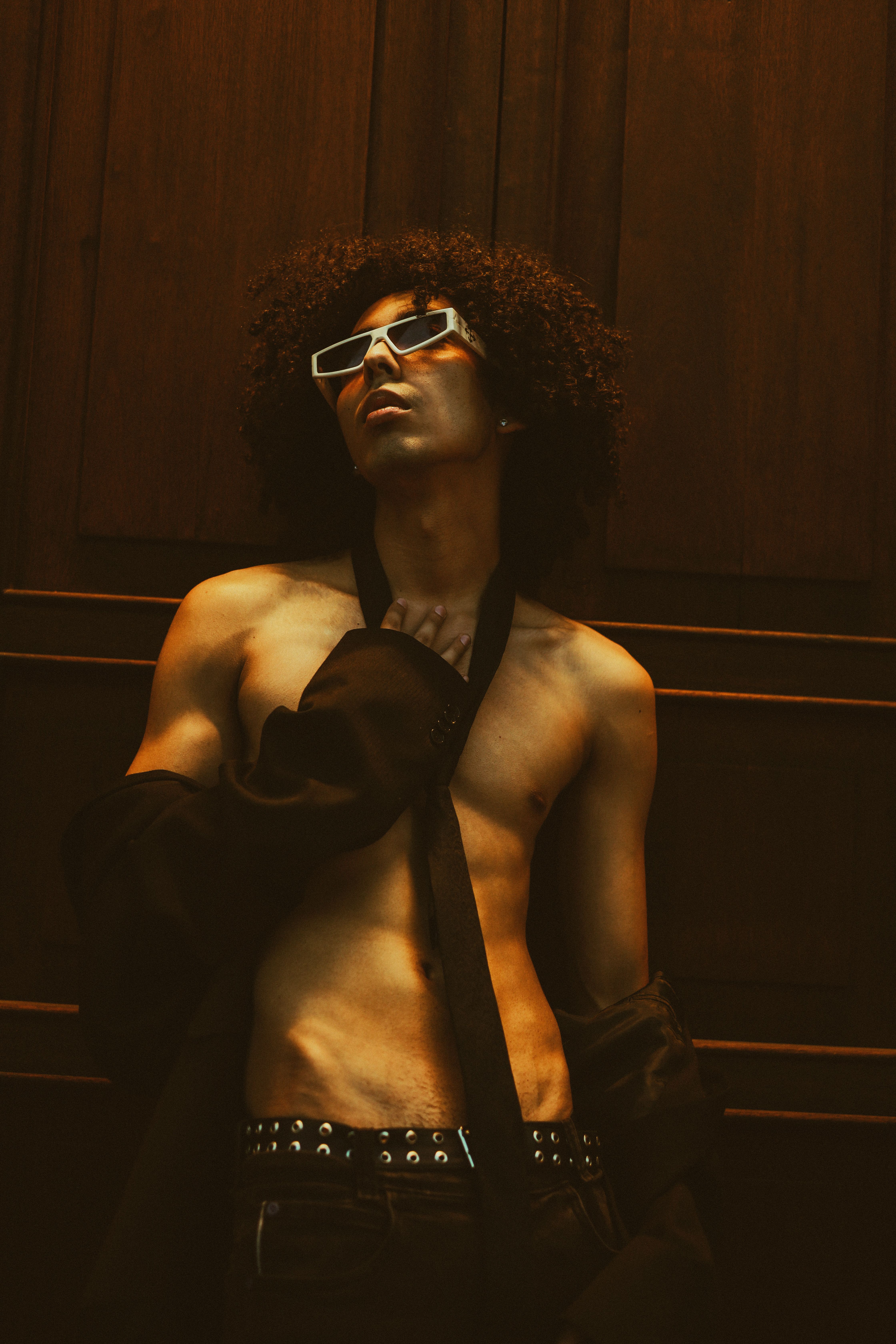 A fashionable young man wearing retro sunglasses poses indoors, showcasing a bold style.