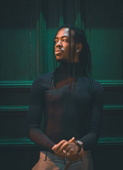 Free A fashionable young man with braided hair against a dark backdrop, exuding confidence. Stock Photo